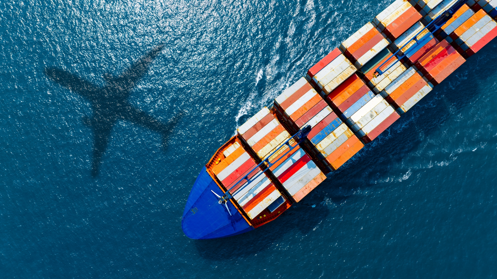 Cargo ship with containers and airplane shadow, symbolizing global trade, tariffs, market volatility, and supply chain disruption.